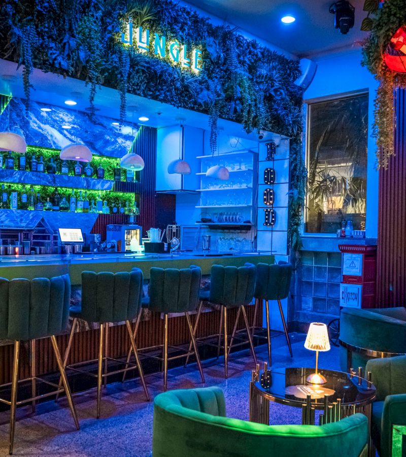 A dimly lit bar with green chairs and blue lighting