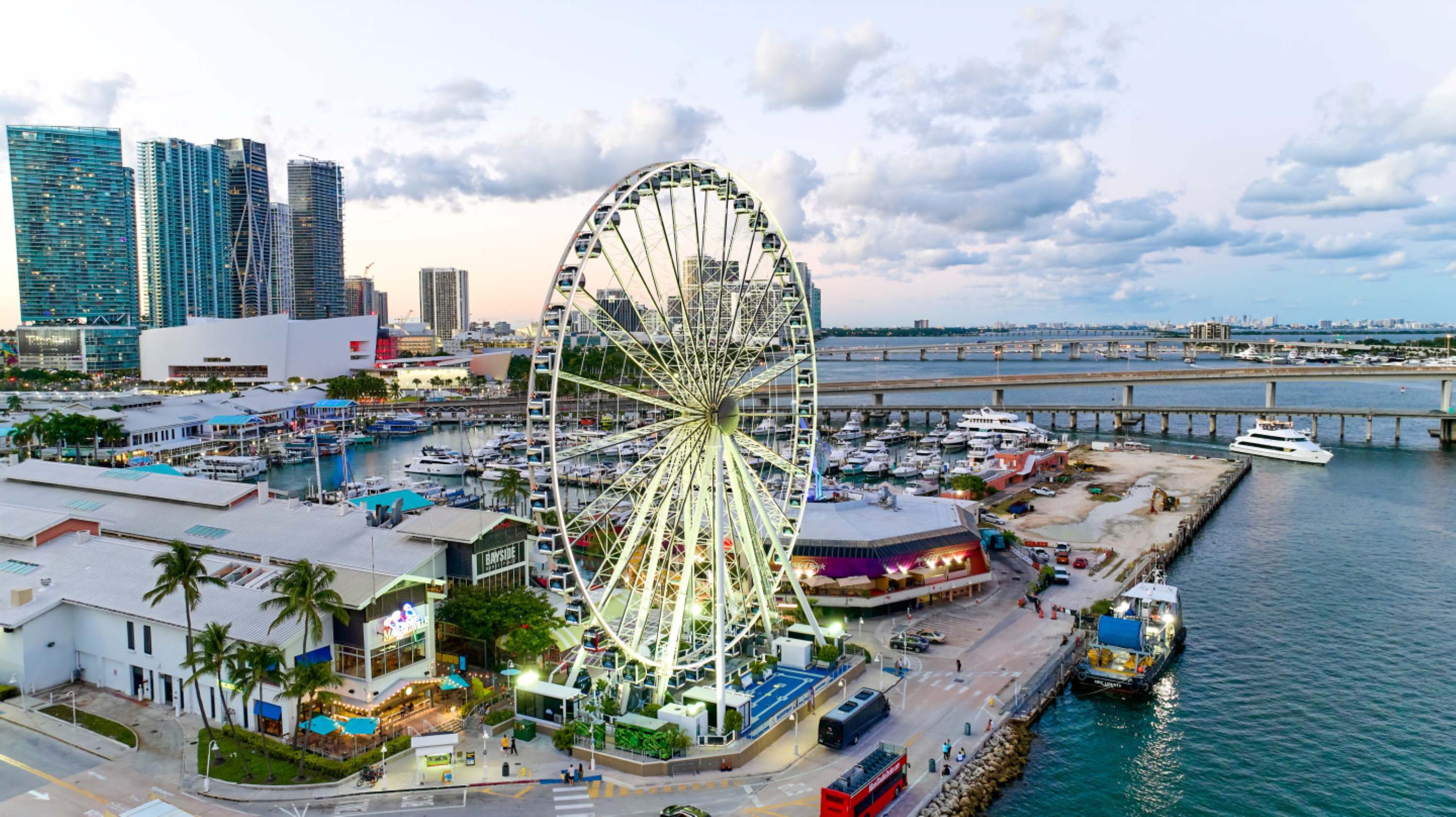 Aerial view of a waterfront area with a large Ferris wheel, boats, and city buildings.