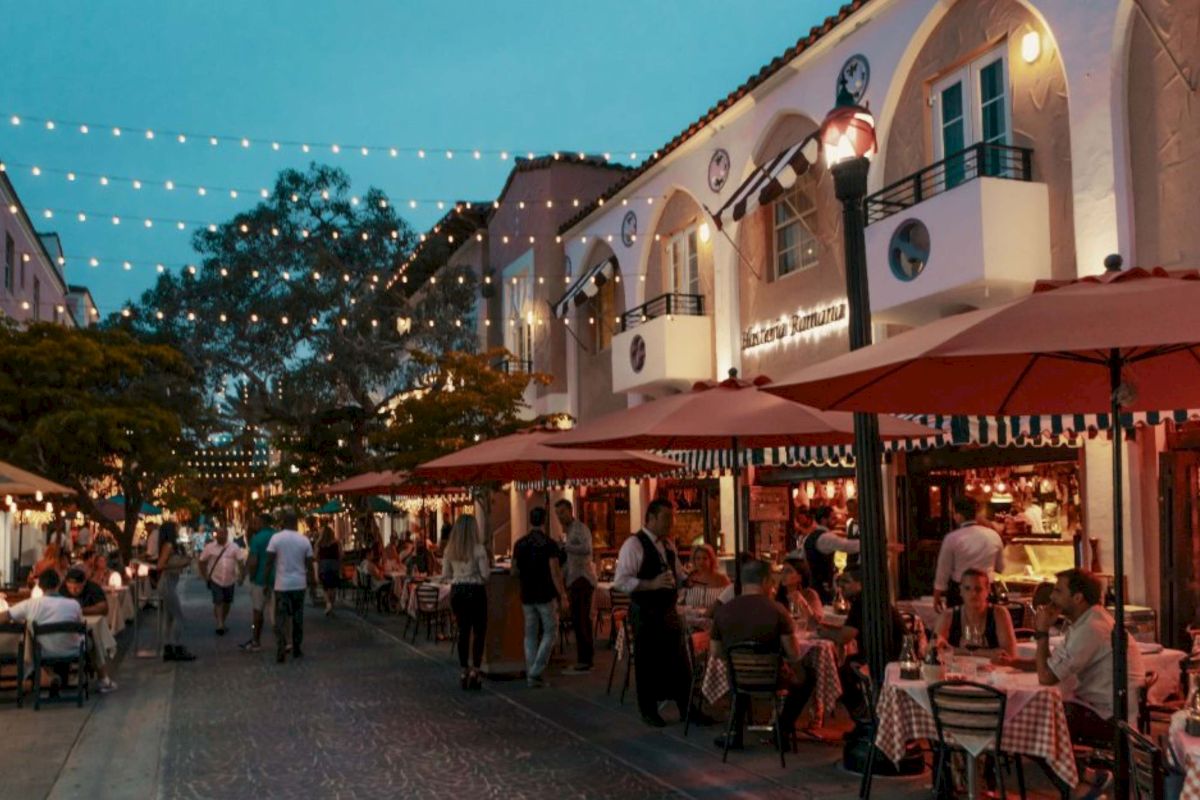 a nighttime view of a restaurant and street with people sitting at tables under umbrellas