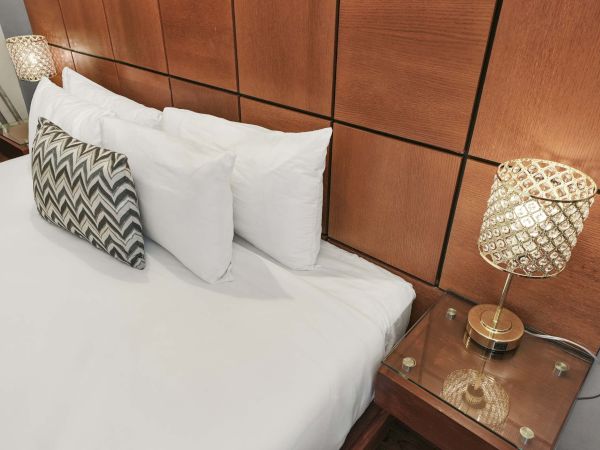 A neatly made bed with white sheets and pillows, a chevron-patterned throw pillow, and two bedside glass lamps on wooden nightstands.