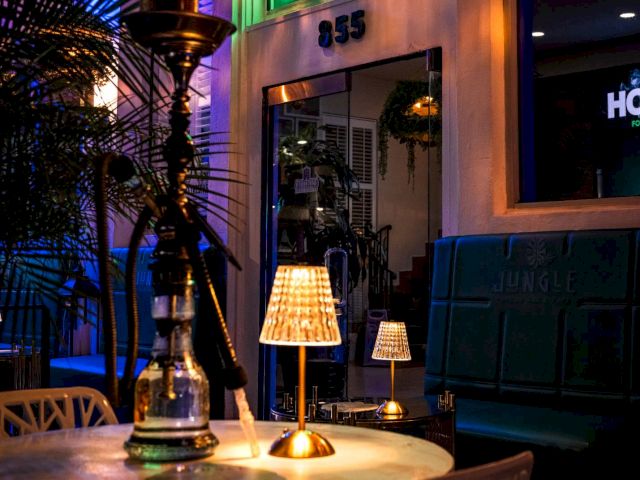 A dimly lit lounge with a table, chairs, and a hookah