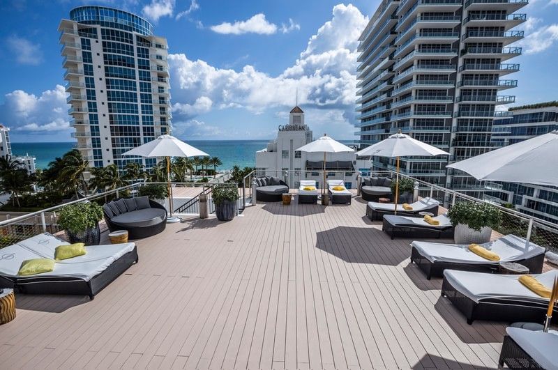 A rooftop pool area with lounge chairs and umbrellas overlooking the ocean and city skyline.