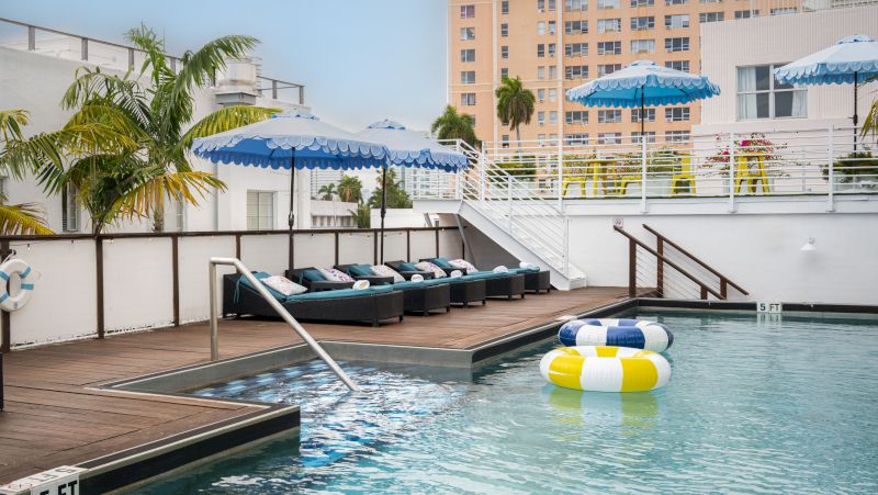 A pool with a wooden deck, lounge chairs, and blue and white umbrellas.